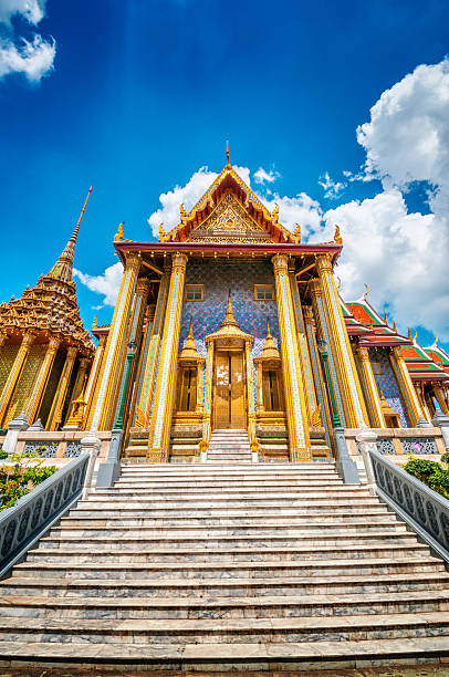 Prasat Phra Thep Bidon in Grand Palace, Bangkok, Thailand "Prasat Phra Thep Bidon in Grand Palace and Wat Phra Kaew Temple interior, Bangkok, Thailand. The Emerald Buddha temple. Visible are two of the many Buddha temple and the Golden Pagoda in interior of Grand Palace. Dramatic cloudscape with blue sky and cumulus clouds over the Grand Palace.See more images like this in:" grand palace bangkok stock pictures, royalty-free photos & images