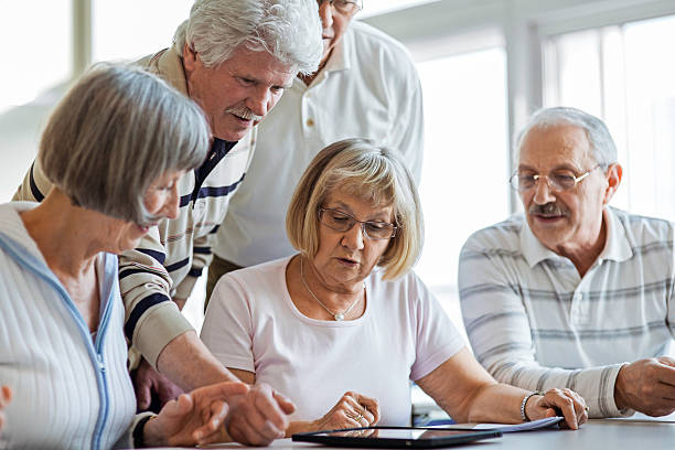 Group of seniors examine digital tablet Group of seniors looking at digital tablet in the classroom. middle age adult studying stock pictures, royalty-free photos & images