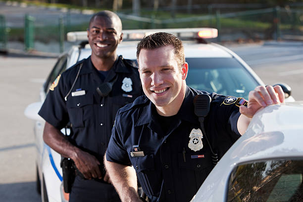 Police officers Multi-ethnic police officers (20s) standing in front of police car. Focus on Caucasian man. police force smiling officer stock pictures, royalty-free photos & images