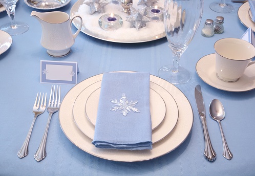 Elegant Christmas or winter Table setting in blue,white and silver. Blue tablecloth, white plates trimmed in silver, silver tableware, blue napkin with crystal snowflake. Horizontal image would be good for Christmas or holiday use.