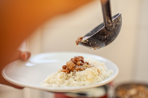 Hands of a young Brazilian man serving a plate of rice and beans for lunch