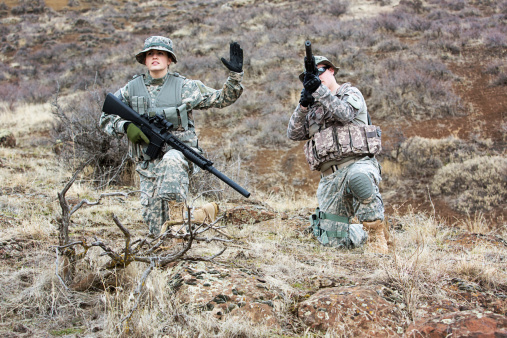 Two American soldiers in the field. Female soldier is signaling to hold fire.