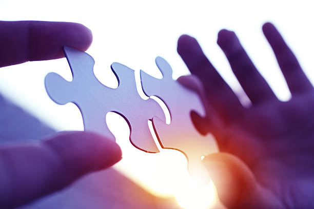 Hands holding two pieces of puzzles, against blue sunset background.
