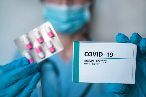 Infectious doctor holding COVID 19 antiviral drug. Coronavirus epidemic. Copy space.