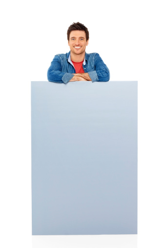 Image of smiling young man standing behind blank billboard over white background