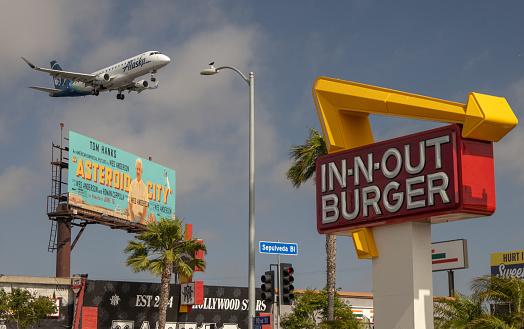 Los Angeles, CA, USA - June 18, 2023: Alaska Airlines Flight approaching LAX airport. In ’n out Burger sign in the foreground.
