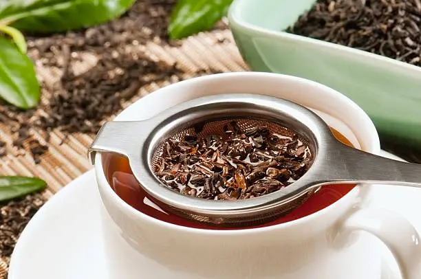 Assam black tea brewing through a tea strainer into a cup and saucer with loose leaf assam tea leaves