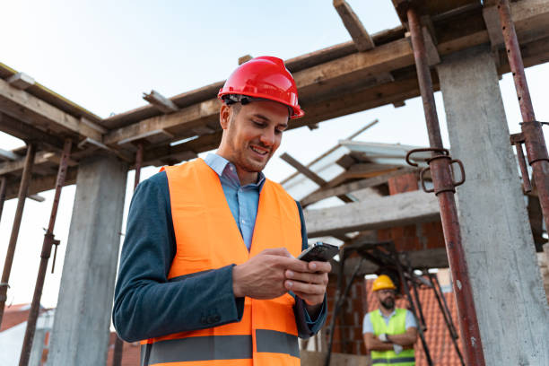 Young male Caucasian building contractor, using mobile phone, on a construction site stock photo