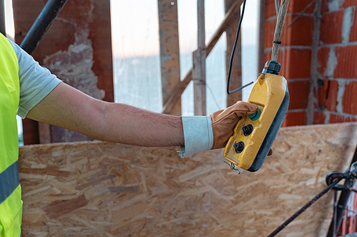 On a construction site, an unrecognizable male Caucasian construction worker, pushing the button on the elevator remote control