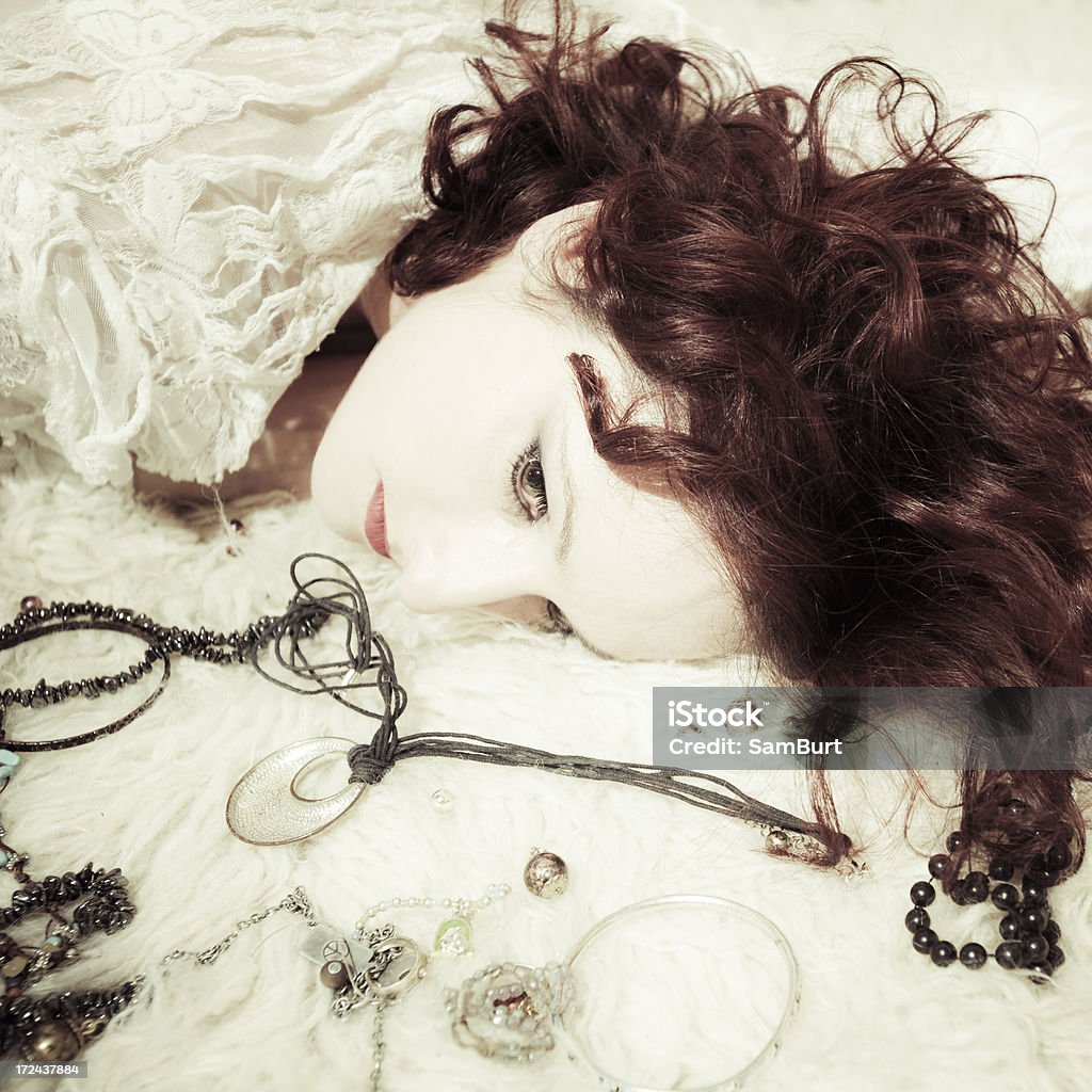 Woman Surrounded in Jewellery A woman in white lace lies on a sheepskin rug holding a knife and surrounded by jewellery. Adult Stock Photo