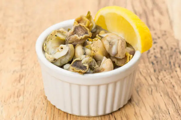 A portion of whelks that are ready to eat with a slice of lemon.