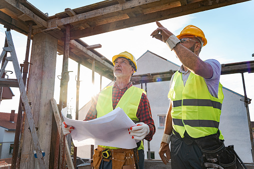 Mid-adult and senior male Caucasian architect and building contractor, having a meeting on a construction site