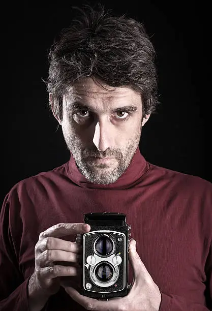 Portrait of a man with 6x6 medium format camera. Shot on black screen in photo studio.