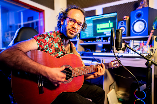 Portrait of a mid adult man playing guitar and recording at music studio