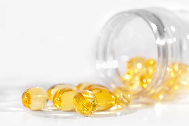 Vitamin gel pills and capsules pouring from a medicine bottle Yellow vitamin gel pills coming out of a transparent medicine bottle, containing various healthy ingredients, including Vitamin E, C and fish oil. On white background with shallow depth of field. cod liver oil fish oil vitamin a pill stock pictures, royalty-free photos & images