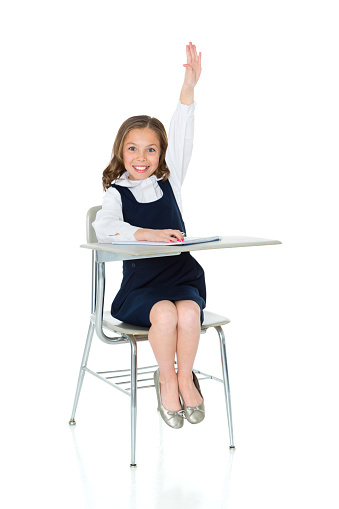 A student with her hand up sitting at a classroom desk.  Isolated on a white background.