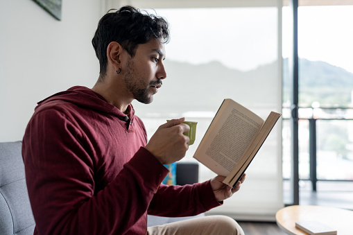Young man reading a book and drinking coffee at home