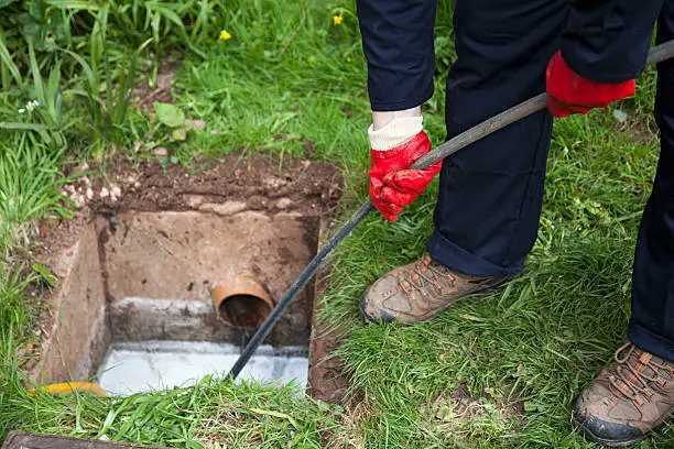 Drain being cleared by worker in navy overalls.