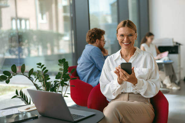 istock Woman freelancer use mobile phone while working on laptop in modern coworking and looks camera 1724415221
