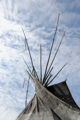 Top of a Native American Tipi against a blue sky filled with altostratus clouds.