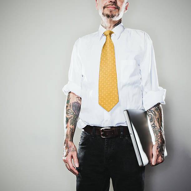 New Professional A business man stands with tattooed arms, a white collared shirt and tie, holding a laptop.  Two forearm sleeve tattoos.  Representing a new generation of modern business standards and style. forearm tattoos men stock pictures, royalty-free photos & images