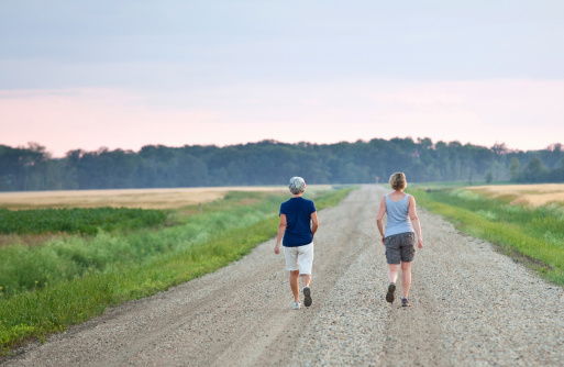 A senior woman and a 30-something woman walking down a gravel road in the country. Horizontal colour image. Prairie setting.