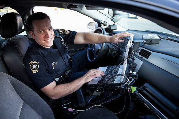 Police officer sitting in cruiser Police officer (20s) sitting in police car, with laptop computer. police car photos stock pictures, royalty-free photos & images