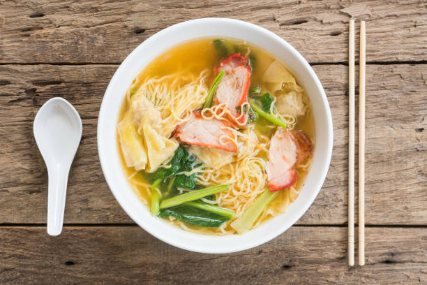 istock Egg noodle soup with red roasted pork in white bowl on wood background, Flat lay composition, Top view 1724449357