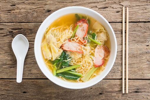 Egg noodle soup with red roasted pork in white bowl on wood background, Flat lay composition, Top view