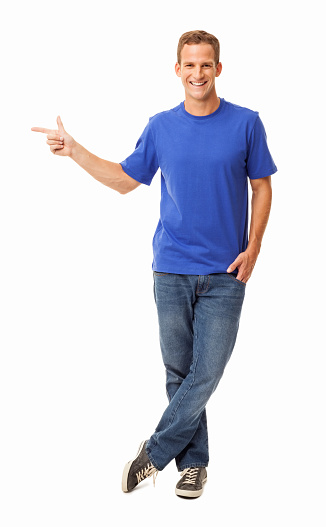 Full length portrait of young man in casual wear indicates something as he points sideways. Vertical shot. Isolated on white.