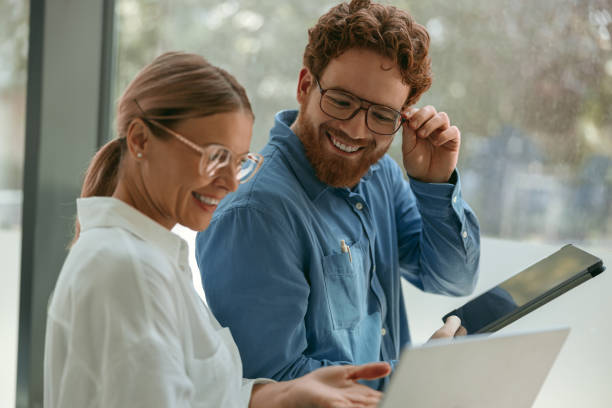 istock Smiling business coworkers working together on project in office while use laptop and digital tablet 1724457382