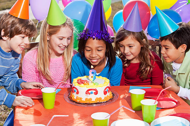 Multi-ethnic children (7-10 years) having fun at birthday party.  Lit candle (number 8) on the cake.