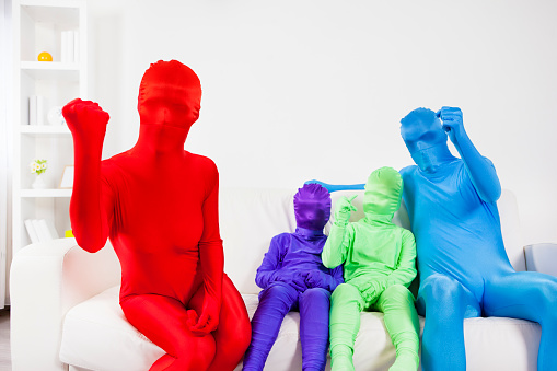 Colorful family in zentai suits watching soccer and enjoy. Family is presented in different colors as unrecognizable people due to stop racism concept in mind. Idea in this series of photo was to simply show people as people without characteristics they can be defended as good or bad, black or yellow or white … So STOP RACISM Selective focus to mother in red.