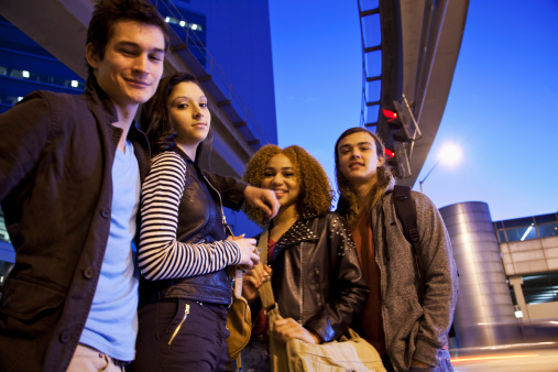 Two young multi-ethnic couples (17-18 years) hanging out in the city at dusk.  Focus on girl on left, with striped sleeve.