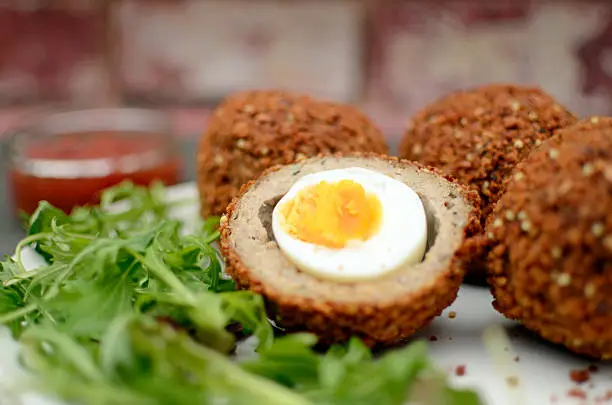 "Free range eggs covered in pork meat with a breadcrumb coating, served with salad and a tomato dip."