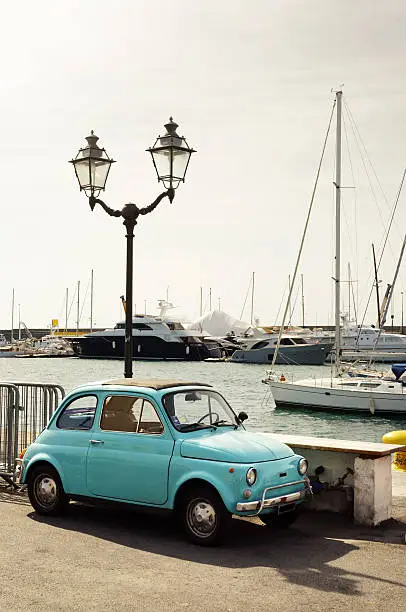 Classic Fiat 500 parked in front of the San Remo marina, Italy. Slightly toned image.