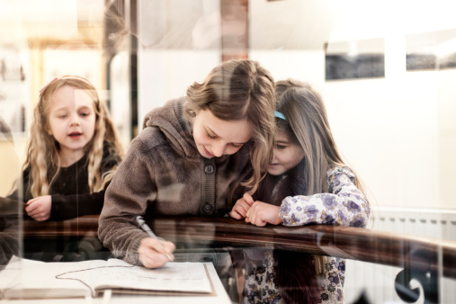 Three young girls filling in an information sheet, at a museum, Lyme Regis, Dorset, UK