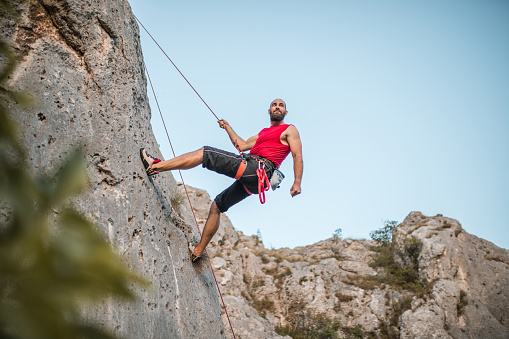 A bearded man climbs a mountain using a special rope and climbing equipment