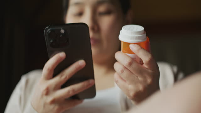 Young Asian woman holding pill bottle checking prescription on pill bottle