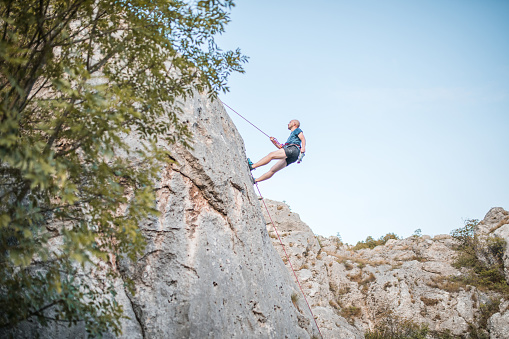 Young man climbing a steep mountain, using climbing equipment.