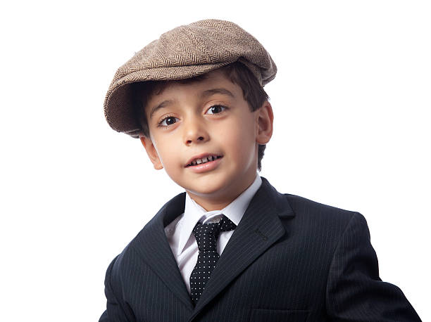 A boy wearing a striped shirt and a denim hat, slightly tipping it, smiles directly at the camera.