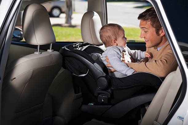 Father putting baby in car seat Young father (20s) putting baby boy (8 months) into car seat (or taking him out). Sc0601 stock pictures, royalty-free photos & images