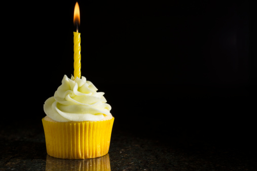 A lemon-lime cupcake with a birthday candle on a black granite countertop with a black background. More of this cupcake: