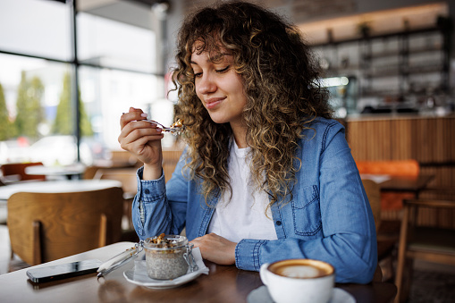 Young happy woman eating chia pudding for breakfast at cafe