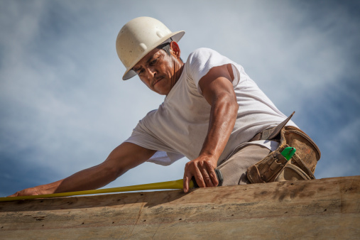 A Hispanic construction worker on a residential construction site in Southwest Florida.  He is on top the top of a concrete wall forming part of the shell of the building.
