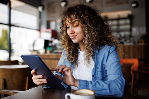 Young smiling woman using digital tablet and enjoying coffee at a cafe