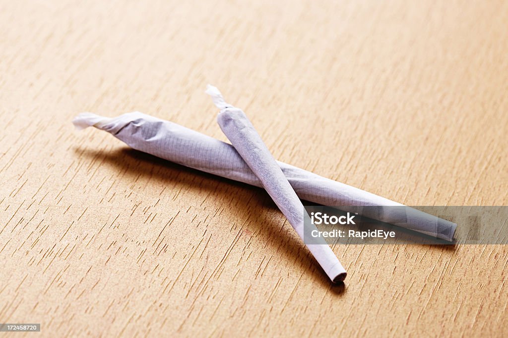 Two marijuana joints, big and small, on wooden surface "On a wooden surface sit two hand-rolled reefers, or joints, of marijuana, one large and one small, ready to smoke." Color Image Stock Photo