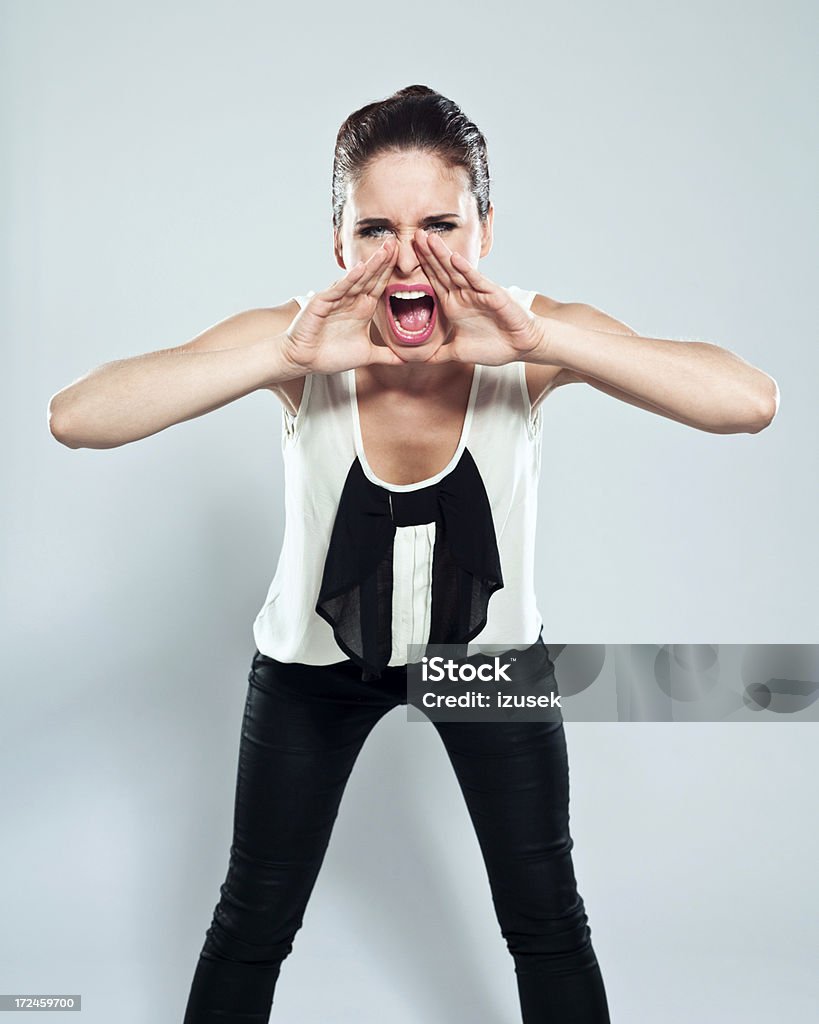 Shout Portrait of young woman shouting at the camera. Studio shot on a grey background. Hands Cupped Stock Photo