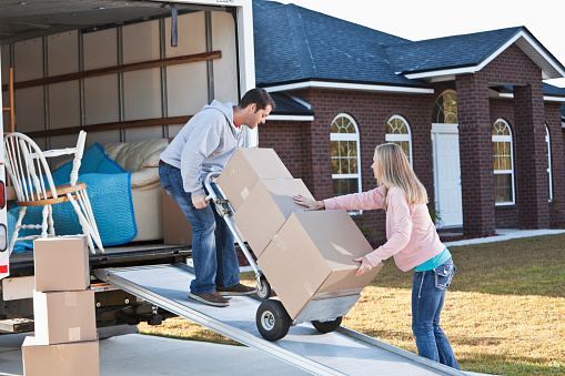 Mid adult couple (30s) unloading moving van.