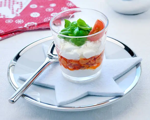 amuse bouche of parmesan cream with red pesto topped with basil and tomato on dining table with Christmas decoration